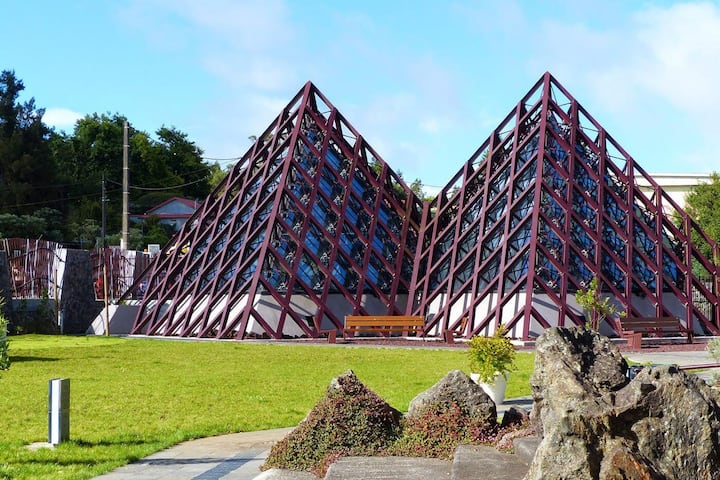 Pyramides vitrées à structure rouge de la Cité du Volcan, entourées de pelouse et de roches
