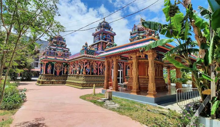 Temple tamoul aux colonnes sculptées dans une cour entourée de végétation tropicale