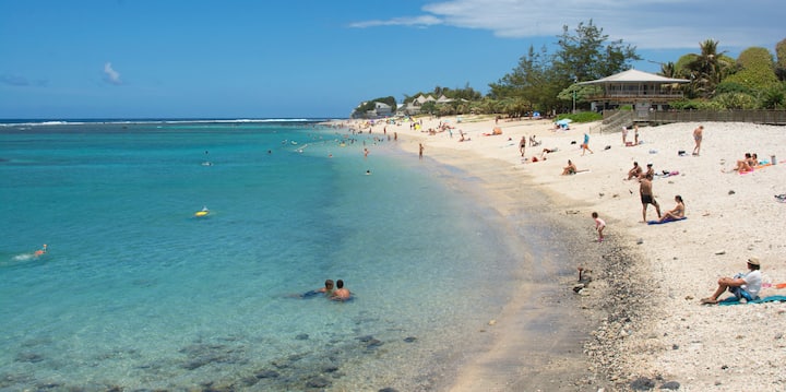 Plage de sable clair bordée d’une eau turquoise avec des baigneurs au bord du lagon