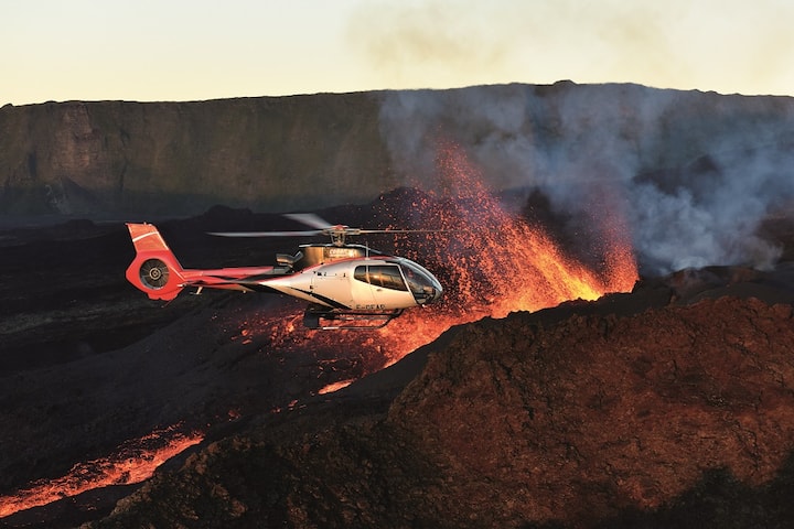Hélicoptère en vol au-dessus d’une coulée de lave incandescente et de projections volcaniques